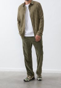 Groen geruit overhemd met knopen over een wit T-shirt, gecombineerd met gestructureerde groene corduroy cargobroek en patroonrijke sneakers.