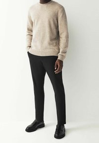 Pull en laine beige à col rond et ourlet côtelé, associé à un pantalon noir slim et des mocassins en cuir noir.
