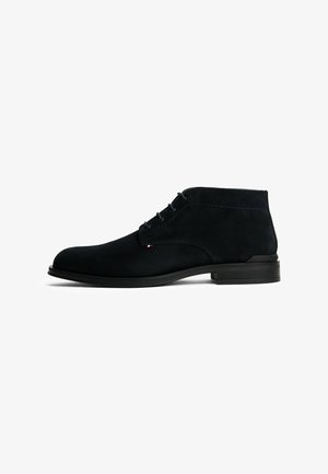 Stivaletto da uomo in suede nero, con punta rotonda, lacci anteriori, tacco basso e piccolo tag del marchio tricolore sul lato.