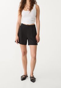 Černé šité šortky s plisováním, kombinované s bílým tílkem. Černé špičaté baleríny se stříbrnými akcenty doplňují celý outfit.