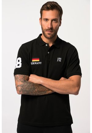 Polo negro de manga corta, con el número "28" en blanco en el brazo izquierdo, bordado "ALEMANIA" y un pequeño detalle de bandera en el pecho.