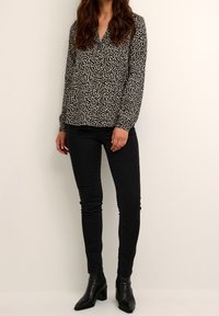 Blouse noire à manches longues avec imprimé floral blanc, décolleté en V, coupe décontractée, associée à un jean skinny noir et des bottines.