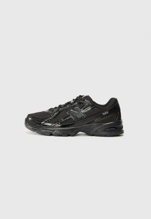 Zapatilla deportiva negra con materiales de malla y sintéticos, que incluye una puntera redondeada, parte frontal con cordones, suela texturizada y detalles reflectantes.