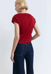 Maglione rosso a maniche corte con orlo a coste abbinato a jeans a gamba larga blu scuro, con cuciture a contrasto e tasche posteriori classiche.