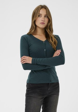 Cardigan lungo a maniche lunghe verde scuro con scollatura a V, bottoni a contrasto sul davanti e un motivo tessile strutturato. Abbinato a jeans neri.