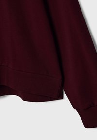 Manche de sweat-shirt bordeaux et ourlet côtelé avec poignet élastique, présenté sur un fond clair.
