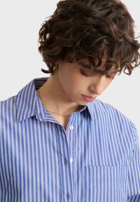 Blue and white striped button-up shirt with a collar, single chest pocket, and smooth fabric texture. Features petite buttons along the front.