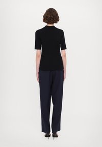 Czarna prążkowana bluzka z krótkimi rękawami, w zestawieniu z luźnymi granatowymi spodniami. Stylizacja zawiera czarne sandały na wysokim obcasie.