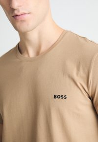 Smeđa pamučna majica s okruglim izrezom i kratkim rukavima, na lijevoj strani prsnog područja s diskretnim crnim izvezenim logom "BOSS".
