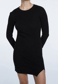 Robe noire en maille côtelée avec des manches longues, un col rond et un ourlet légèrement asymétrique. Texture douce et silhouette ajustée.