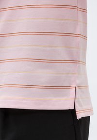 Απαλό ροζ ύφασμα με λεπτές οριζόντιες πορτοκαλί και κίτρινες ρίγες, με ραμμένη άκρη, πλευρική σχισμή, φορεμένο πάνω από μαύρο παντελόνι.