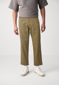 Khaki bomuldsbukser med lige pasform og sidelommer. Kombineret med hvide sneakers og en grå tekstureret top.