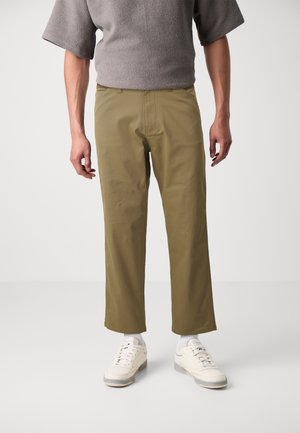 Khaki cotton trousers with a straight cut and side pockets. Paired with white sneakers and gray textured top.