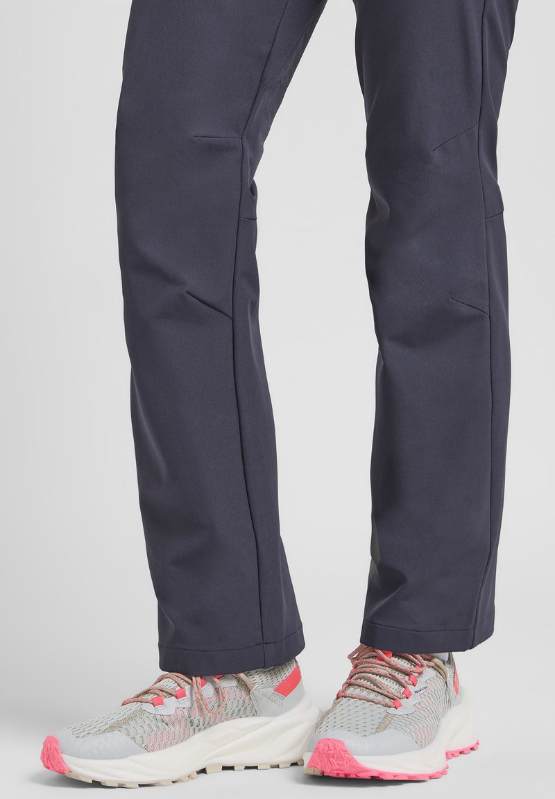 Baskets grises légères avec des accents roses et une tige en mesh, assorties à un pantalon bleu marine doté de jambes ajustées et d'une couture minimale.