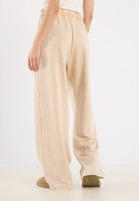 Beige vide bukser laget av myk stoff, med elastisk linning og sidesømmer. Designet for en avslappet passform.