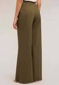 Pantalones de pierna ancha en verde oliva hechos de una tela suave, con cintura alta y silueta ajustada. Diseño minimalista sin adornos visibles.