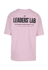 Heled roosa lühikeste varrukatega T-särk, mille seljal on must tekst "LEADERS' LAB" ning "PEAK PERFORMANCES - ORIGINAL 030 PRODUCT - EST. 2006."