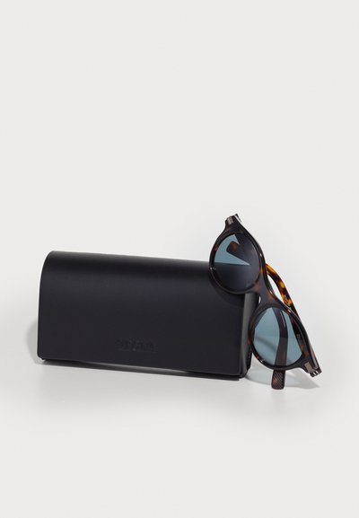 Tortoiseshell sunglasses with blue lenses resting on a black rectangular case. The frame features rounded shapes and textured accents.