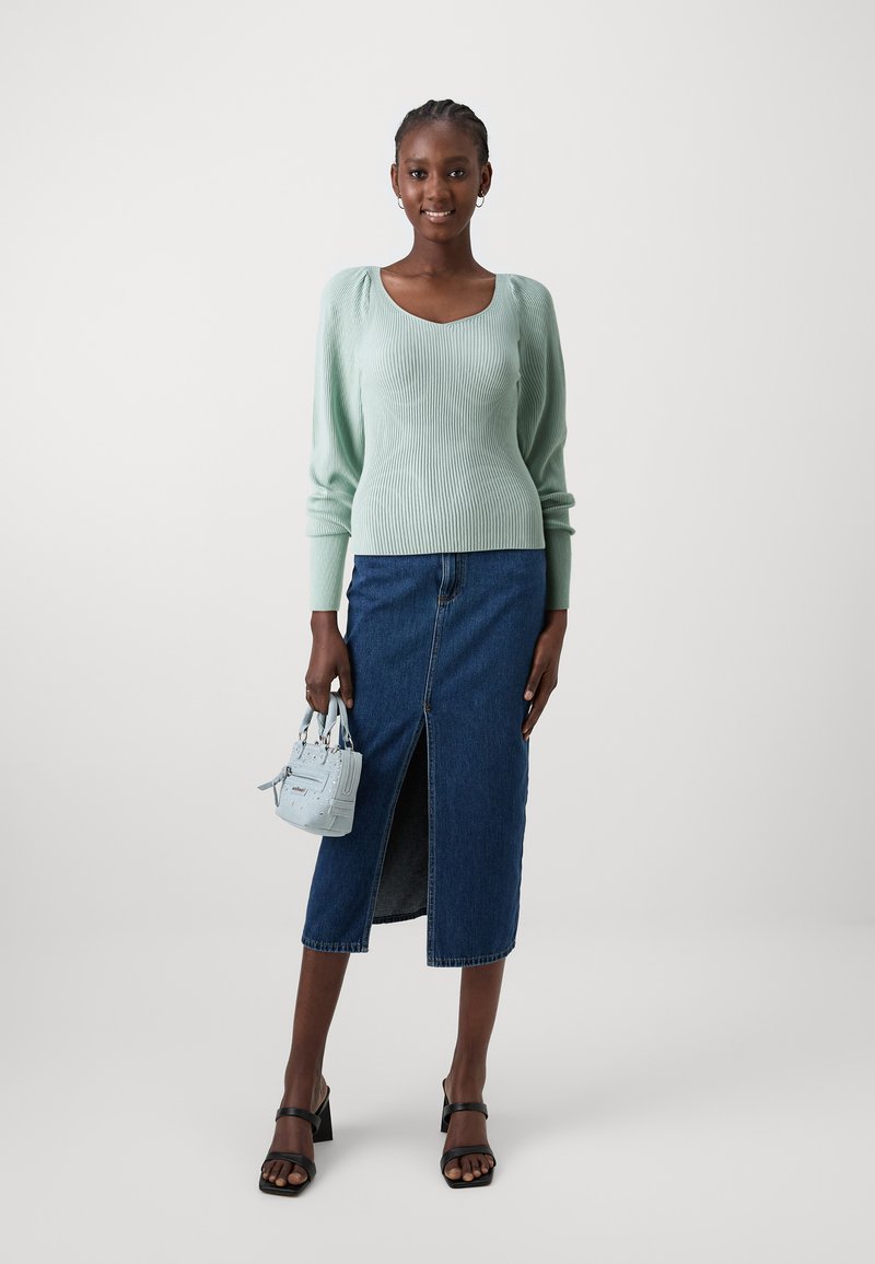 Pullover a coste verde chiaro, gonna midi in denim scuro con spacco frontale, sandali neri con tacco a blocco e una piccola borsa azzurro chiaro.