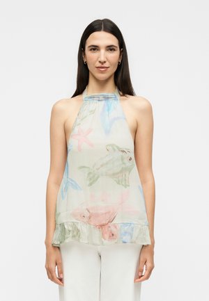 Mladá žena, ktorá má na sebe tielkový halter top s pastelovými potlačami rýb a morských hviezd, v kombinácii s bielymi nohavicami, stojaca na jednoduchom pozadí.