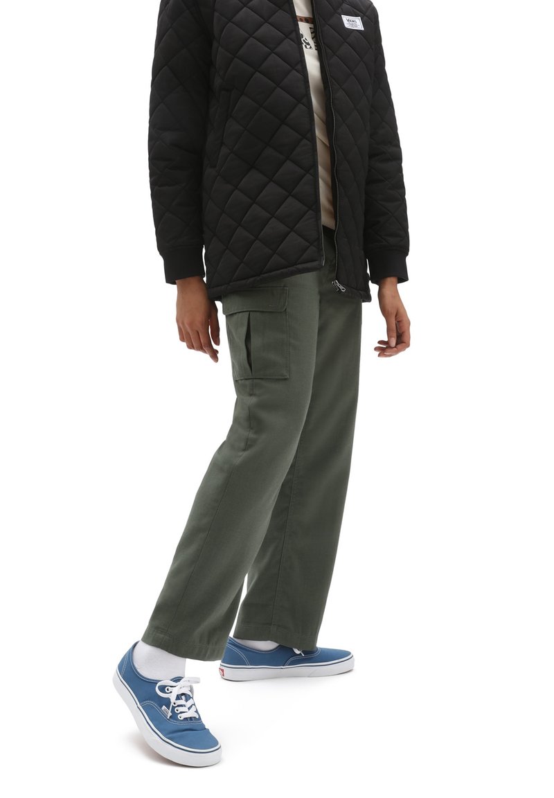 Chaqueta negra acolchada con puños de canalé, pantalones cargo verde oliva con bolsillos laterales y zapatillas de lona azules con cordones blancos.