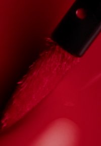 Helle rote Nagellack mit einem breiten, flachen Pinsel; glänzende Oberfläche; glatte Textur; Hintergrund in einem leicht dunkleren Rotton.