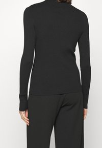 Pull en tricot noir à côtes avec des manches longues et un col montant, présentant une texture lisse et une coupe ajustée. Pas de décorations visibles.