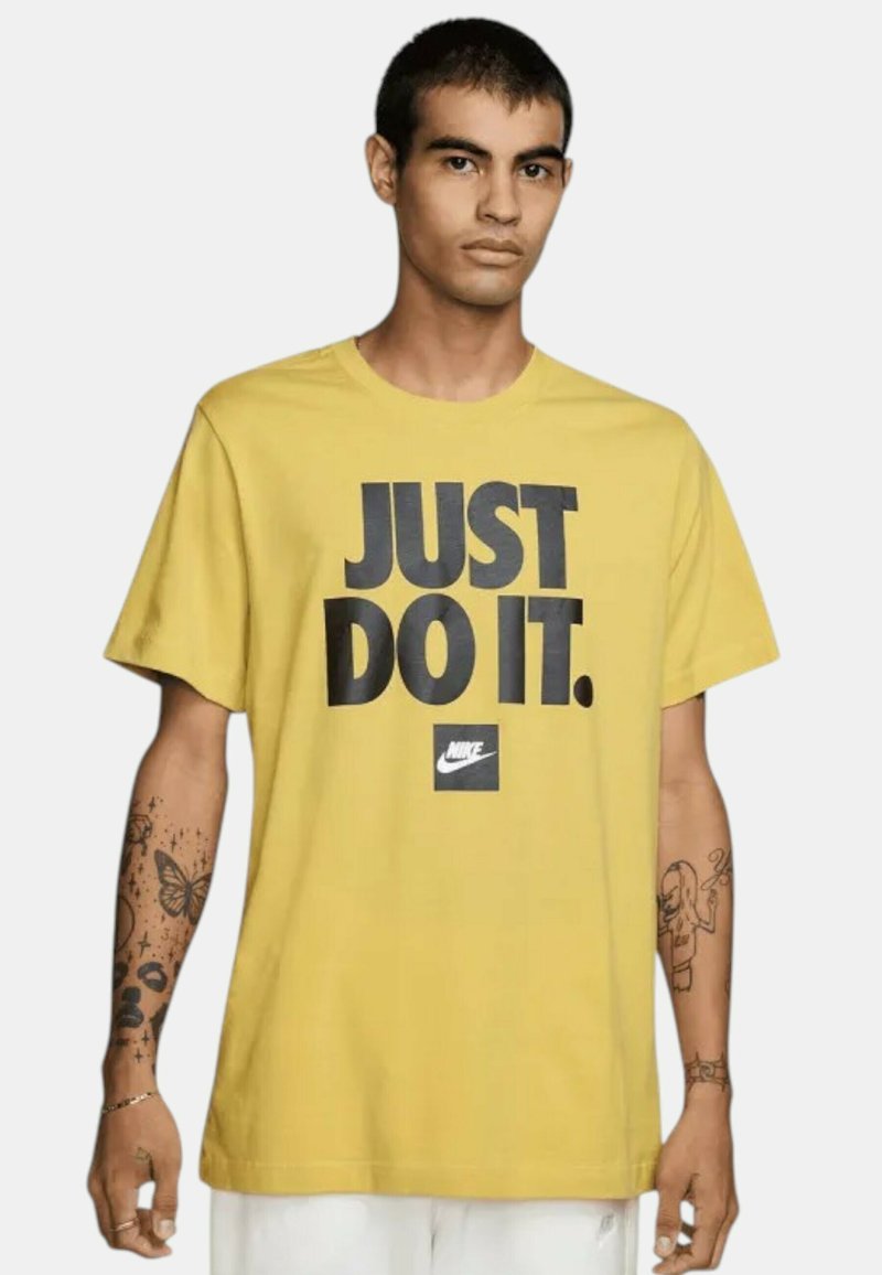Camiseta amarilla de Nike con el emblemático texto negro "JUST DO IT." en negrita, logotipo cuadrado en el dobladillo, mangas cortas y un corte relajado.