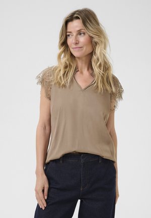 Beige short-sleeve top with lace trim on shoulders, V-neckline, and flowing design, paired with dark blue denim pants.