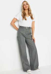 Grå vida cargo-byxor med sidofickor, hög midja med bälte och en slät tygtextur, kombinerat med en vit t-shirt med v-ringning.