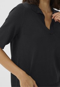 Polo noir en tricot avec un col à revers, des manches courtes et une coupe décontractée. Présente des détails côtelés au col et à l'ourlet.