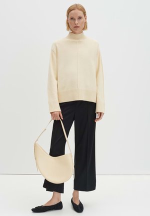 Roomkleurige coltrui met geribbelde zoom, gecombineerd met zwarte wijde broekspijpen en platte zwarte schoenen, met een gebogen beige handtas.