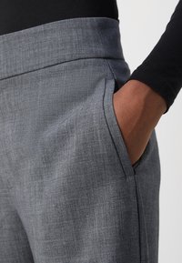 Pantalons en tissu gris avec une finition texturée, dotés de poches latérales et d'une taille haute, présentés à côté d'un haut noir à manches longues.