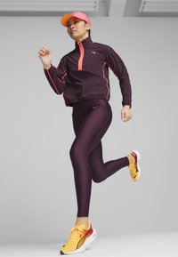 Veste de sport violette avec des accents rose fluo, assortie à un legging violet et des chaussures de course jaunes avec un design dégradé.