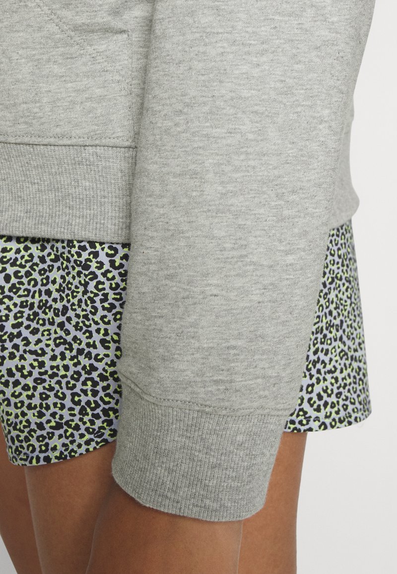 Sudadera gris con puños acanalados combinada con una falda que presenta un estampado de leopardo en negro y verde sobre un fondo claro.