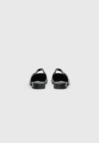 Par crnih kožnih slingback balerinki s niskim složenim potpeticama viđenih odostraga na jednostavnoj bijeloj pozadini.