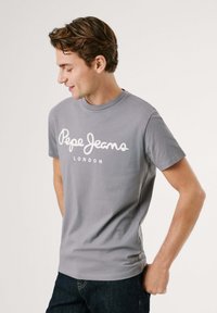 Šedé tričko s krátkým rukávem z bavlny, s bílým logem "Pepe Jeans" a textem "LONDON" potištěným na přední straně. Kulatý výstřih a přiléhavý střih.
