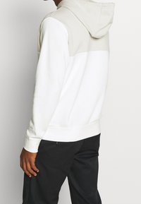 Huvtröja i vitt och ljusgrått, med en färgblockdesign, mjukt tyg, ribbade muddar och en känguruficka.