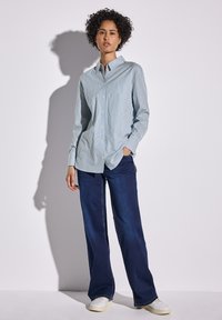 Camicia button-up a righe blu e bianche con colletto, abbinata a jeans larghi blu scuro e sneakers bianche. Tessuto di trama liscia.