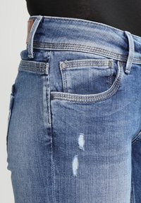 Sinisen farkkukankaan farkut, joissa on klassinen leikkaus, kevyitä kulumia, viisi taskua ja erottuva tikkaus saumoissa.