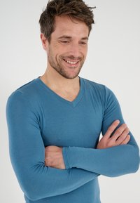 Maglietta a maniche lunghe con scollo a V in un morbido tessuto azzurro chiaro. Presenta un design aderente e una texture liscia. Nessun motivo o stampa visibile.