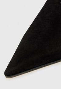 Crne sude cipele s šiljastim prstom, glatke teksture, s elegantnom siluetom i tankim crnim đonom. Nema vidljivih metalnih dijelova ili ukrasa.