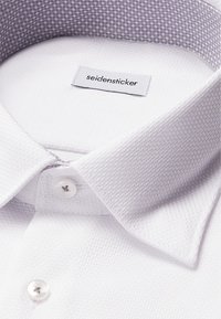 Camicia bianca in tessuto con colletto grigio a motivo. La chiusura anteriore presenta bottoni bianchi. L'etichetta reca la scritta "seidensticker".