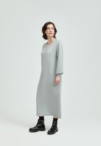 Langes, graues, gestricktes Kleid mit rundem Halsausschnitt und Ballonärmeln, kombiniert mit schwarzen Knöchelstiefeln mit einer klobigen Sohle.