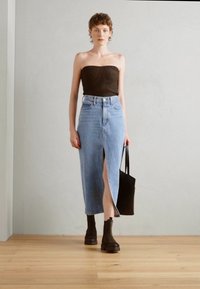 Top marron sans bretelles, jupe midi en denim bleu avec une fente à l'avant, associée à des bottines noires et un sac fourre-tout noir, sur un sol en bois.