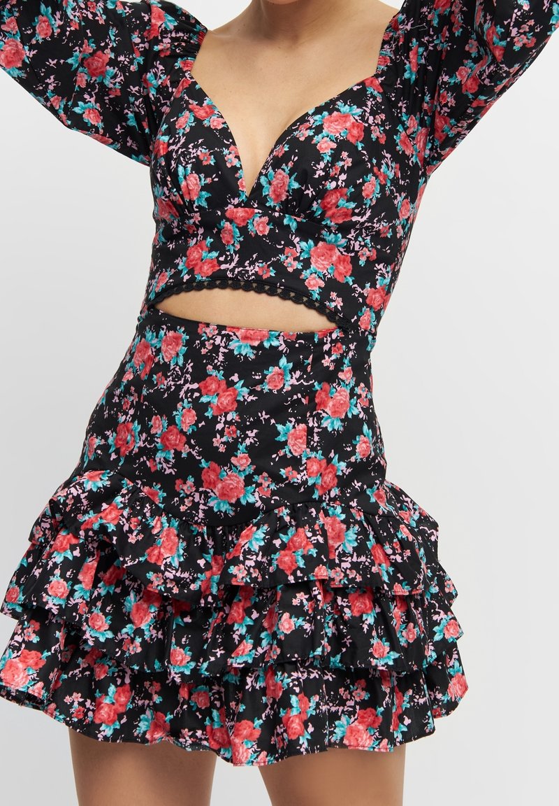 Kvinna som bär en svart blommig crop top med puffärmar och matchande volangkjol i tre lager, med ett midriff-cutout.