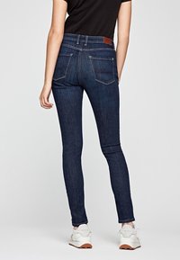 Úzké džíny z tmavého modrého denimu, se zvýšeným pasem, pěti kapsami a minimálními švy. Nosit s černým tričkem a bílými teniskami.