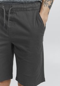 Shorts légers gris foncé avec une taille élastique, un cordon de serrage ajustable, une poche latérale et un ourlet propre.