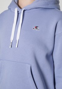 Light blue hoodie made of cotton blend, featuring a front pocket, white drawstrings, and a small logo on the chest. Smooth texture.