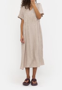 Abito beige lungo fino al ginocchio con maniche corte, scollatura a V e motivo sottile. Abbinato a sandali scuri con fasce larghe e suola spessa.